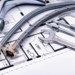 Close-up of plumbing tools and faucet on top of an architectural blueprint, perfect for hardware and construction themes.